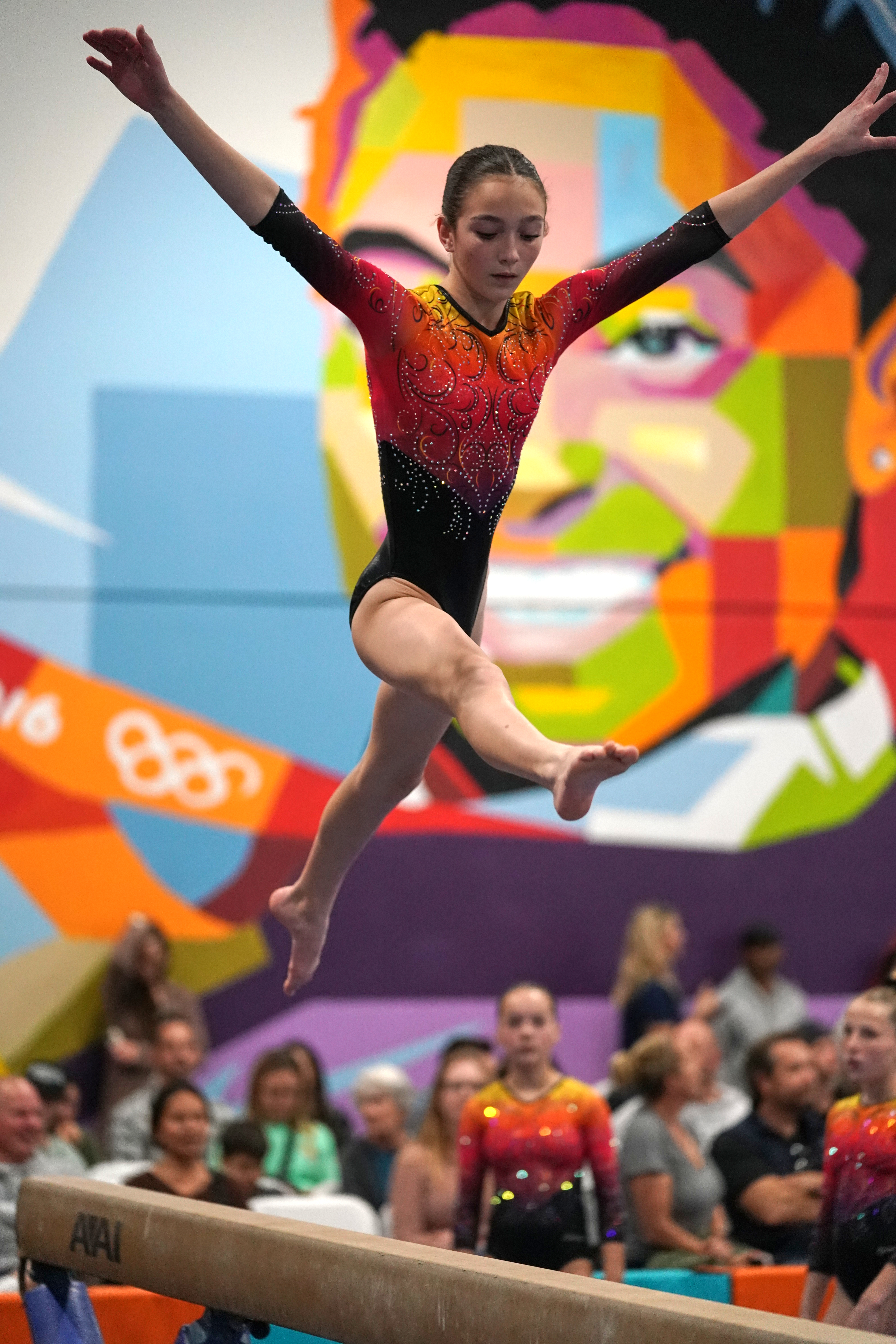 A gymnast leaps above the beam with arms out.